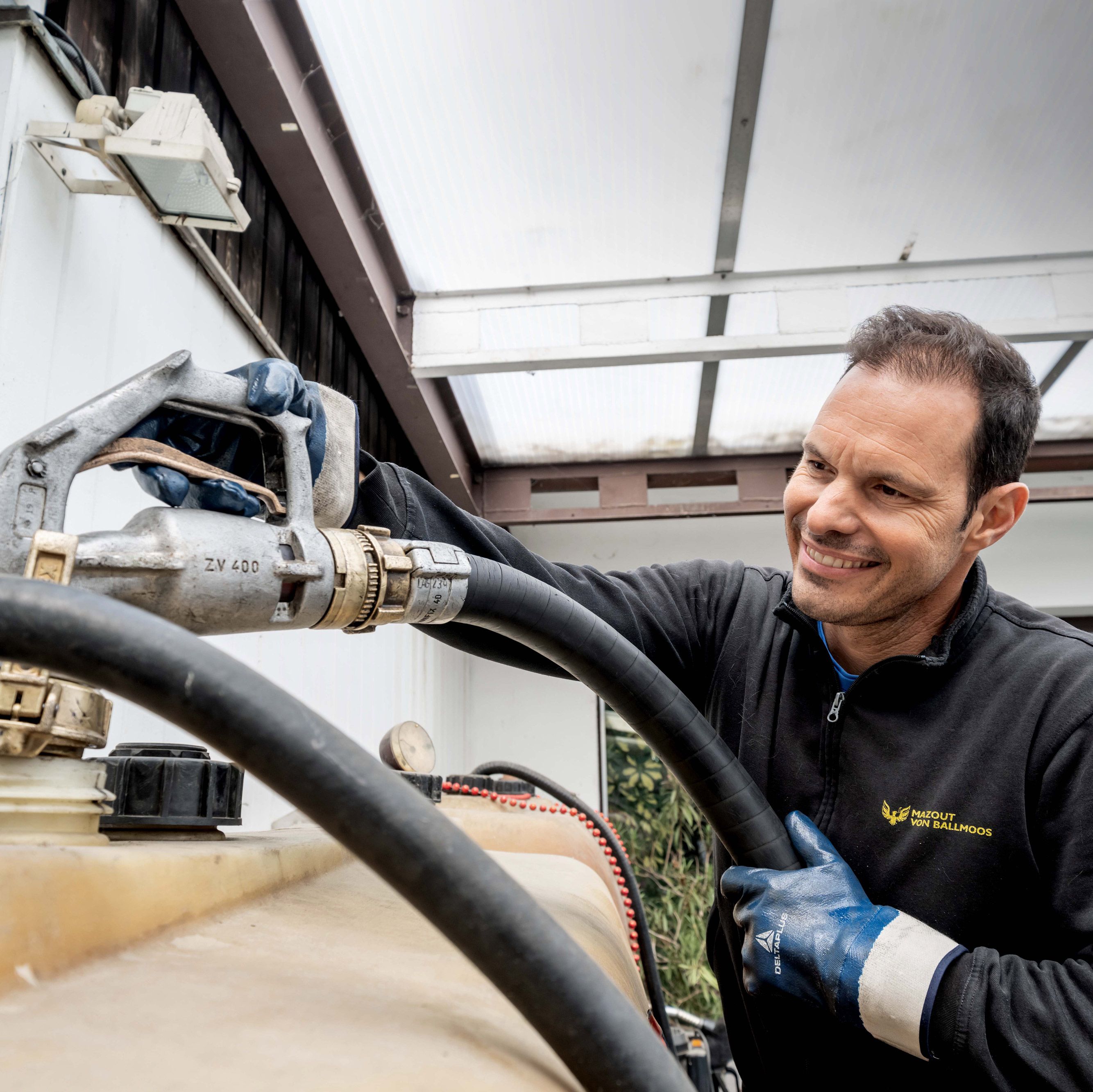 Fröhlicher volenergy Mitarbeiter in Schutzkleidung füllt mit einem Tankschlauch einen Tankkanister auf