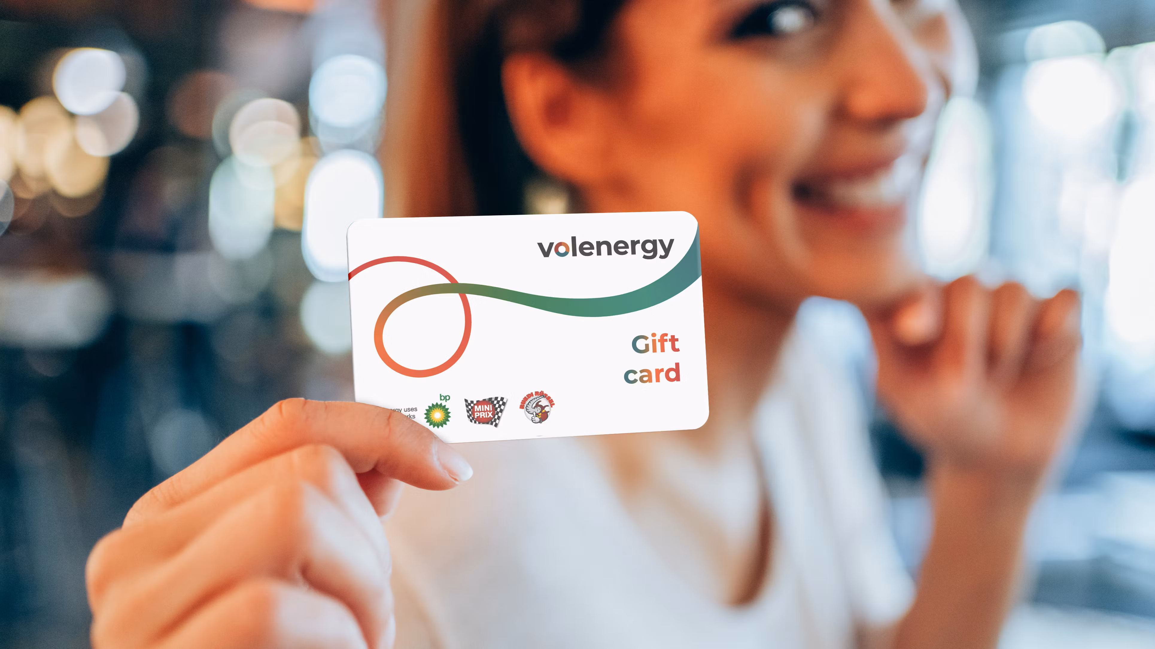 A cheerful woman smiles as she holds up the volenergy gift card for the camera