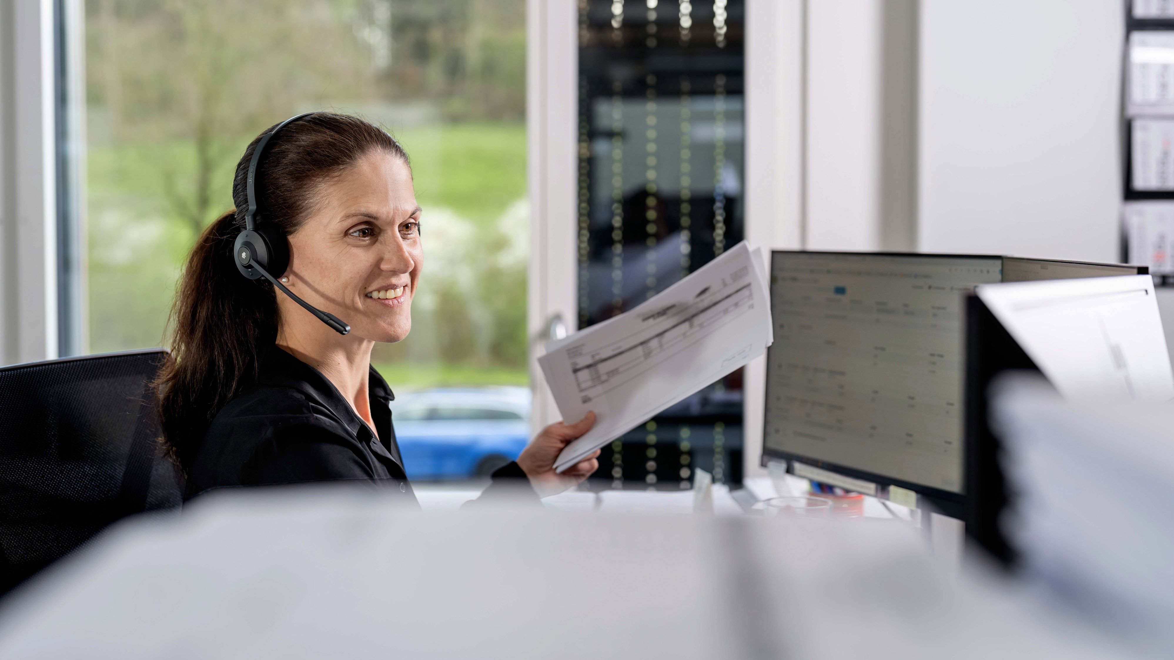 Cheerful volenergy employee takes a call in her office, wearing a headset