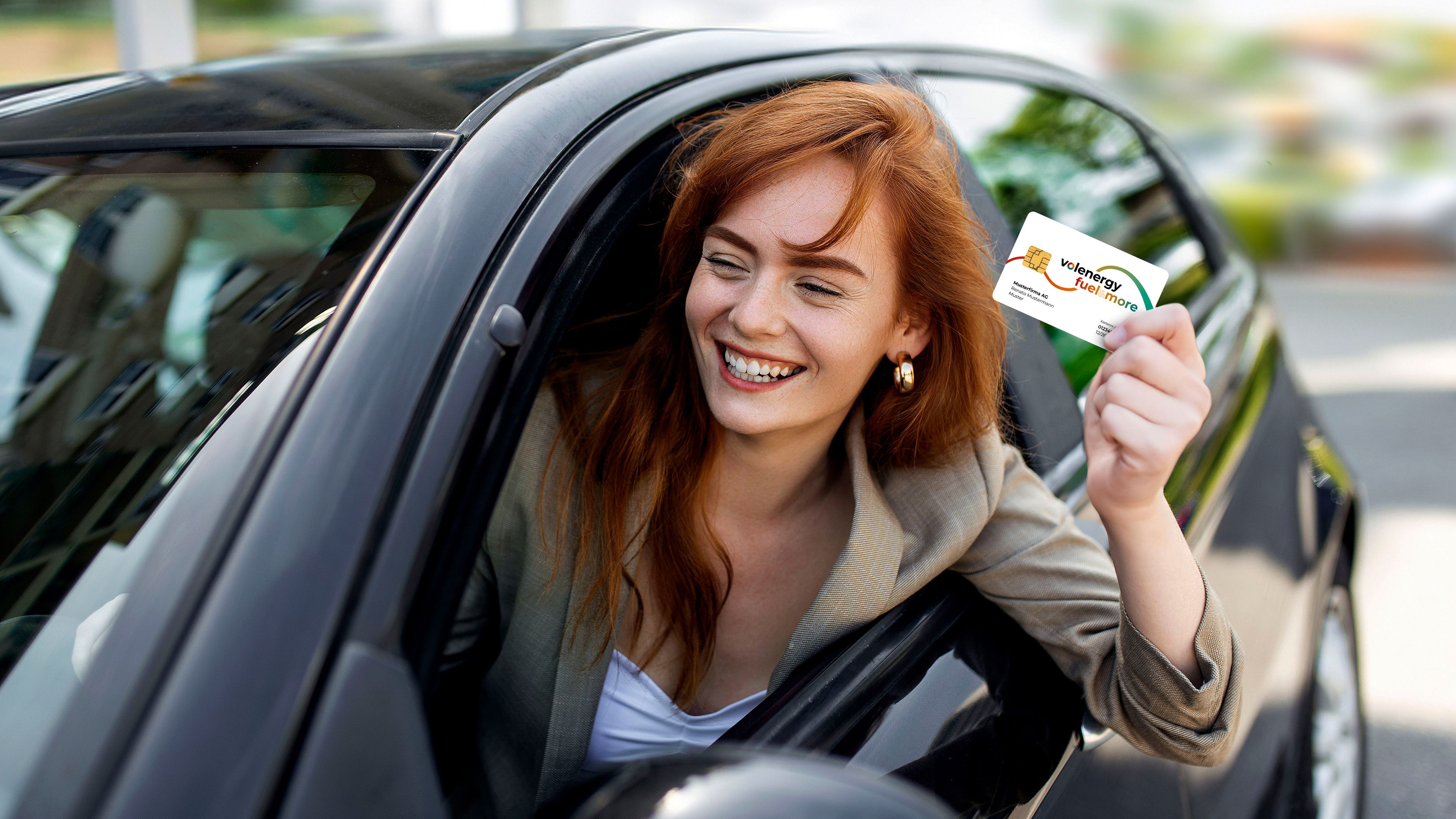 Une femme souriante se penche par la fenêtre de sa voiture en montrant la carte de carburant «fuel & more» de volenergy